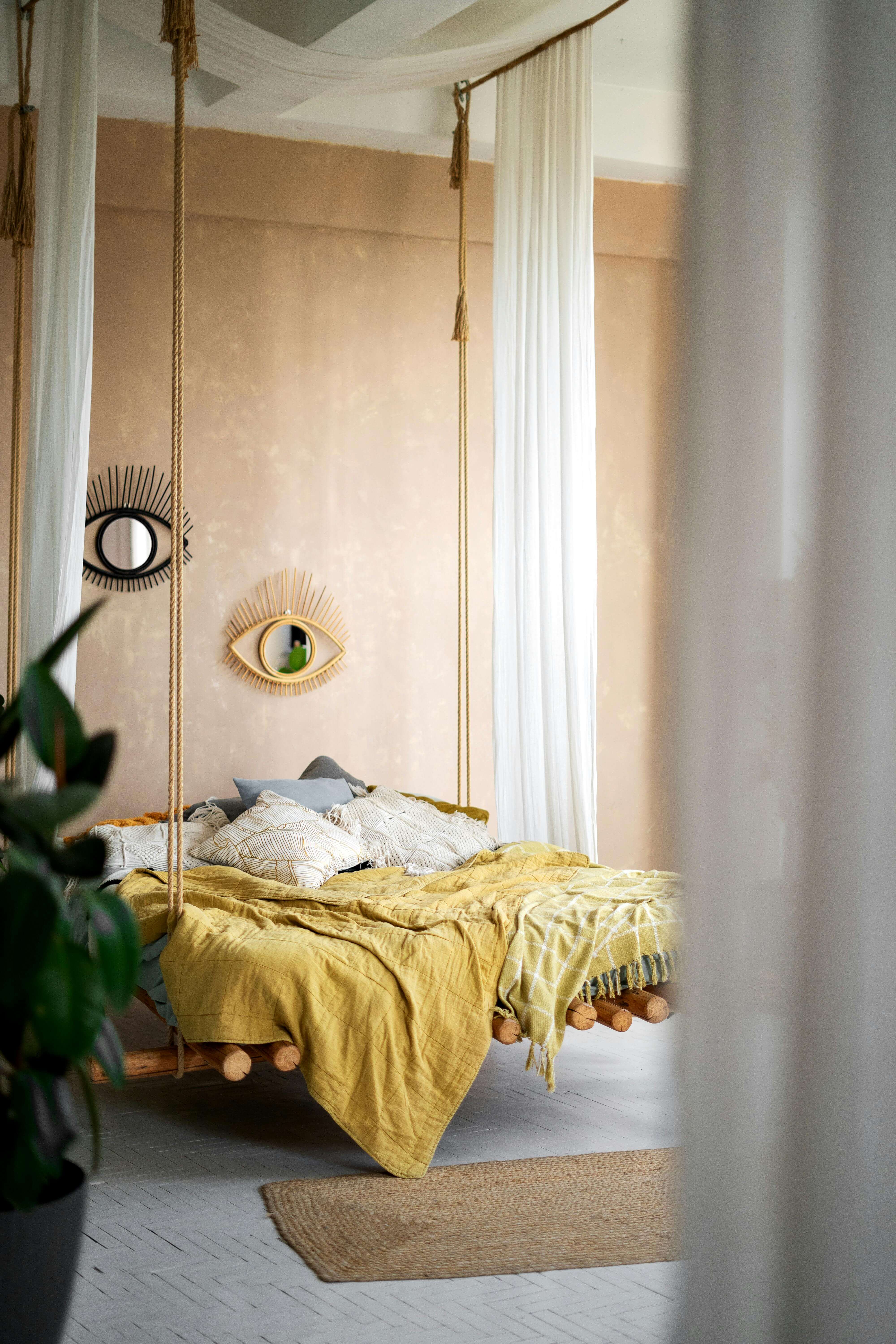 modern boho bedroom with hanging bed, yellow bedding and two eye-shaped mirrors on the wall